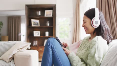 Video-of-smiling-biracial-woman-with-dark-hair-using-headphones-and-smartphone