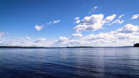 Zeitraffer-Des-Wassers-Auf-Einem-See-In-Finnland-Mit-Vorbeiziehenden-Weißen-Wolken-Und-Einem-Vorbeifahrenden-Boot-In-Der-Ferne