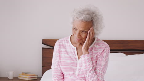 Depressed-Senior-Woman-Looking-Unhappy-Sitting-On-Side-Of-Bed-At-Home