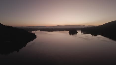 Amanecer-En-El-Borde-Del-Lago-Con-Colinas-Al-Fondo