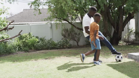 african american father and son play soccer outdoors