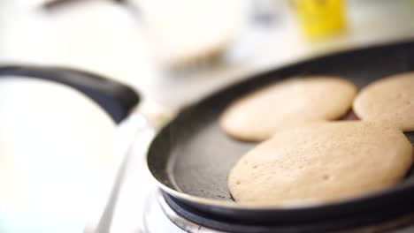 three pancakes are fried in a frying pan, on an electric stove, against the background of the kitchen table.