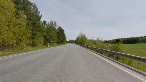 As-the-cars-journey-along-the-road,-they-are-accompanied-by-the-verdant-foliage-on-either-side,-signaling-the-arrival-of-the-summer-season-and-enveloping-the-landscape-in-a-vibrant-atmosphere