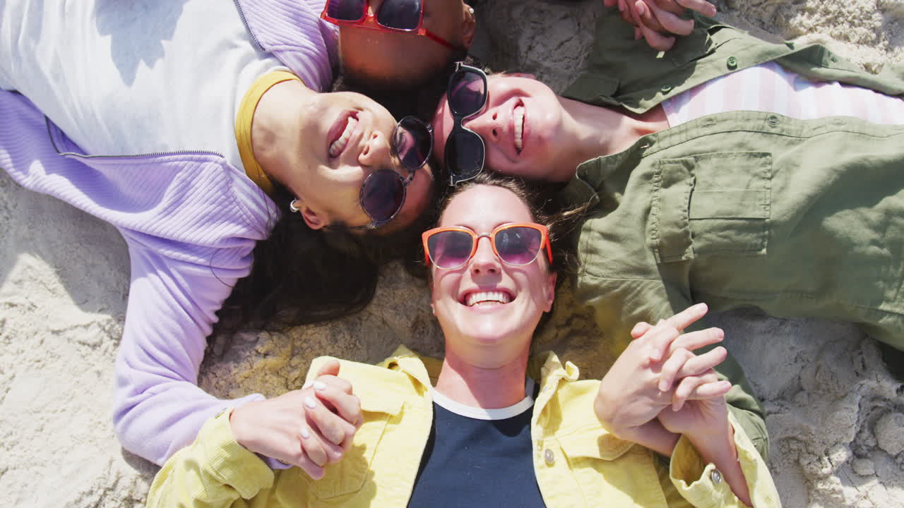 un grupo feliz de amigas diversas divirtiéndose, tomándose de la mano y sonriendo en la playa