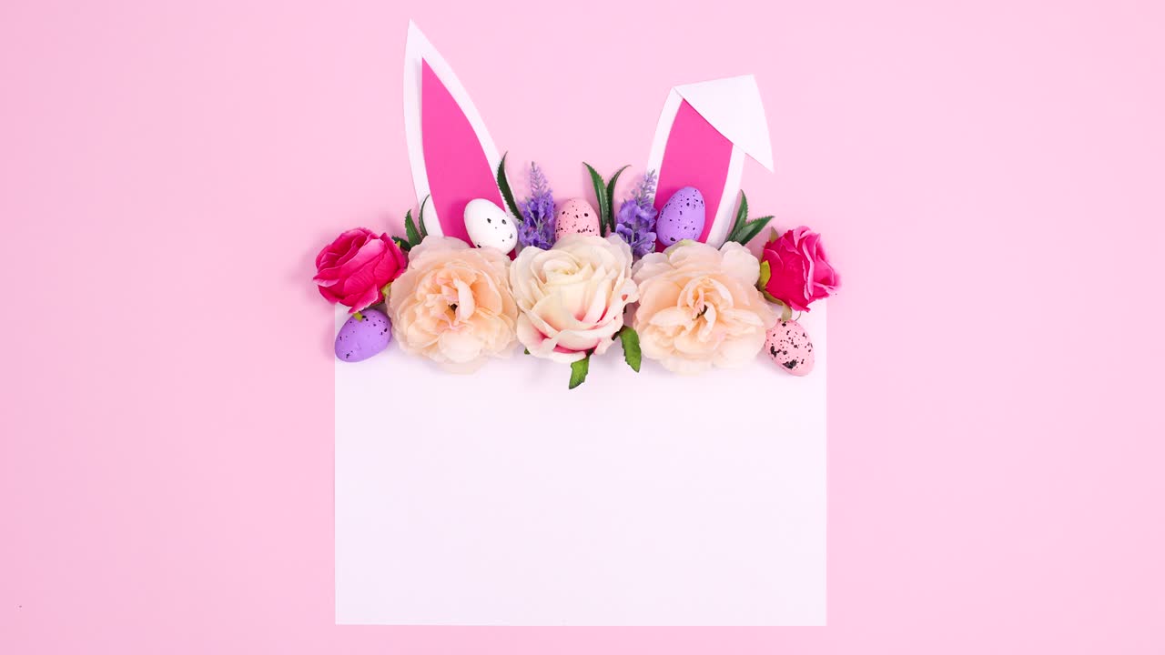 파스텔 분홍색 배경에 종이 카드 메모에 토끼 귀와 함께 움직이는 부활절 꽃 배열.