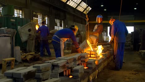 Worker-pouring-molten-metal-from-container-in-foundry-workshop-4k