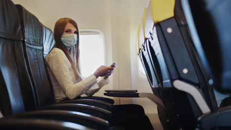 woman wearing a mask and using a smartphone on an airplane