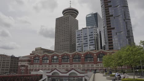 people sitting near waterfront station building, harbour centre tower and skyscrapers, downtown vancouver, british columbia, canada