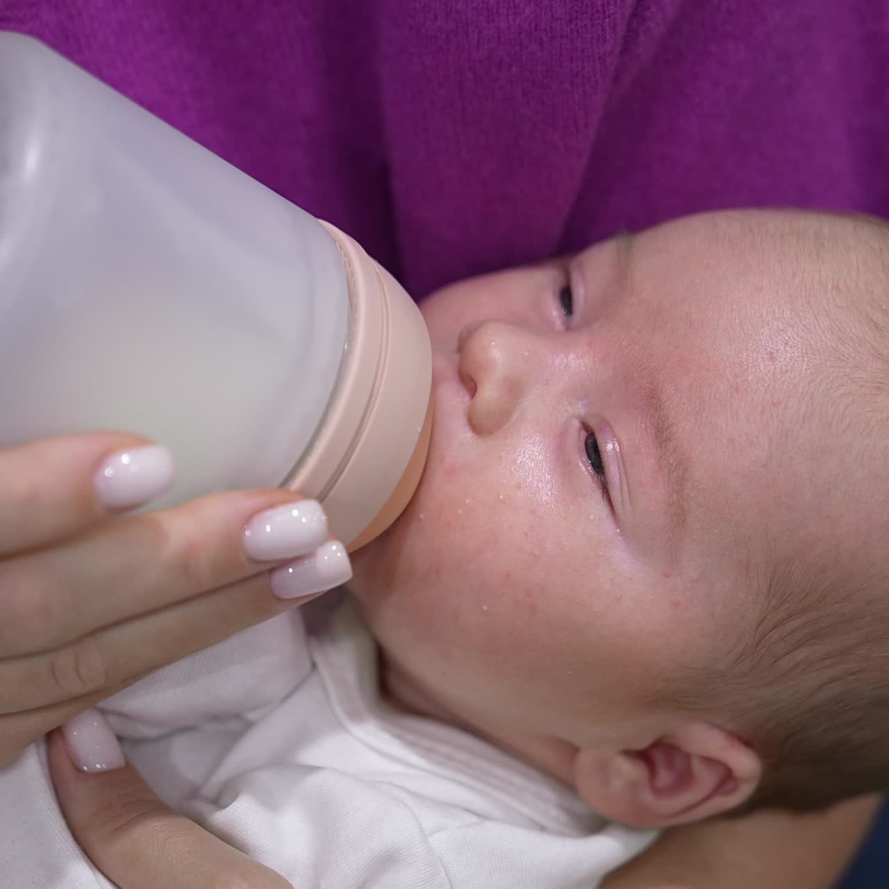 Beautiful newborn boy resting in mother's hands and being fed from a bottle. Little child closing eyes and gradually falling asleep. Close up