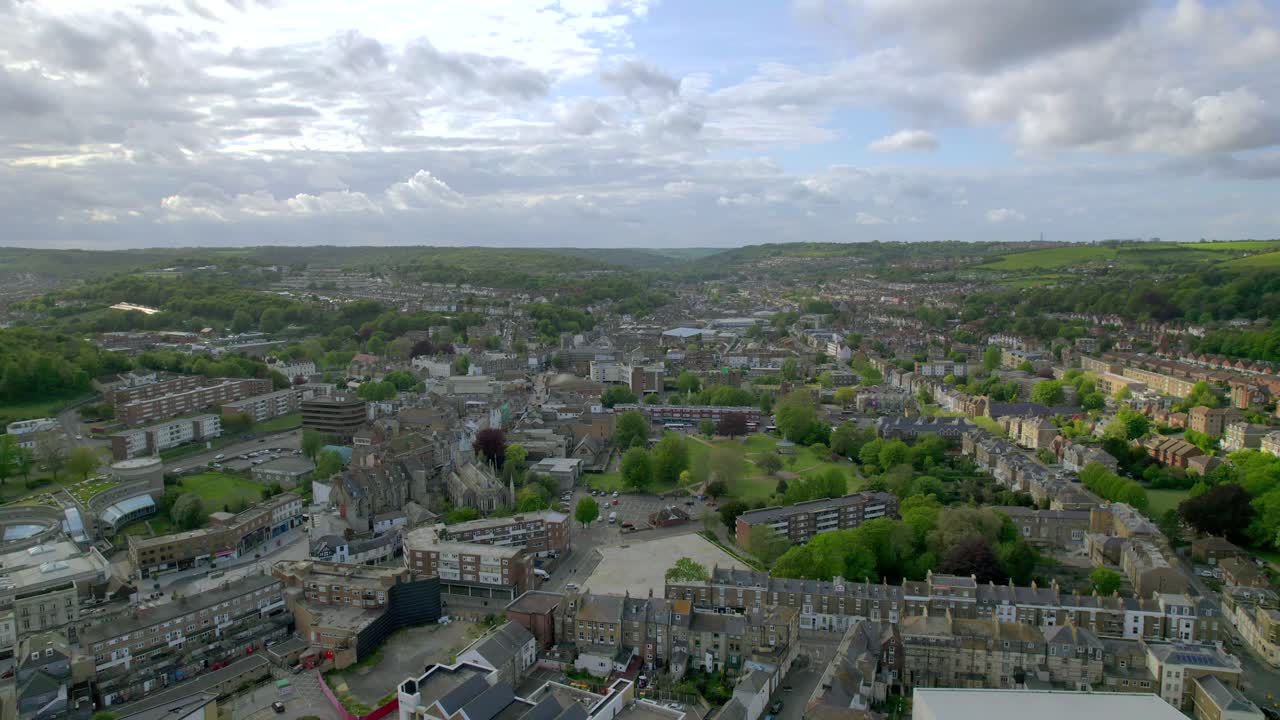 일부 구름이 가득한 하늘 아래 주거 건물, 푸른 공원, 주변 언덕과 함께 도버의 공중 도시 풍경을 보여주는 드론 영상