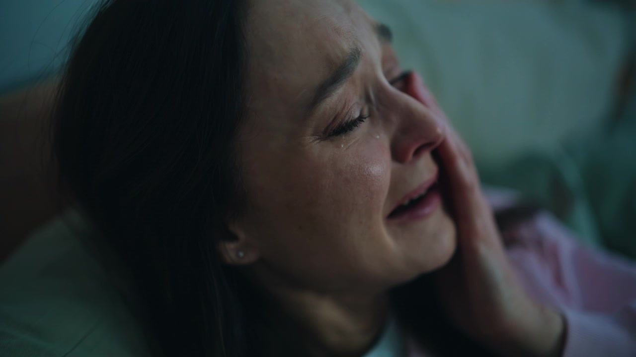 Closeup woman crying bitterly sitting bed late evening alone. Tears stream down
