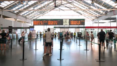 wide shot of passengers arriving at the main terminal hall of alicante train station and going through luggage security checks in alicante, spain.