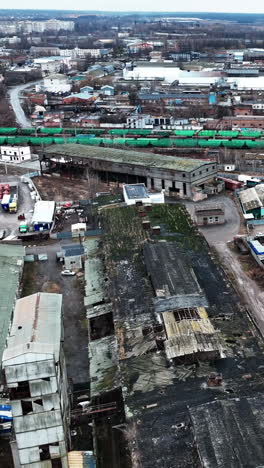 huge industrial territory abandoned long ago. aerial view of old ruined warehouses near railways and trains. city view at the backdrop. vertical video