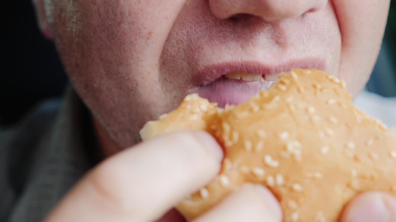 배고픈 남자가 햄버거를 열심히 먹고 프레임에 입만 보입니다.