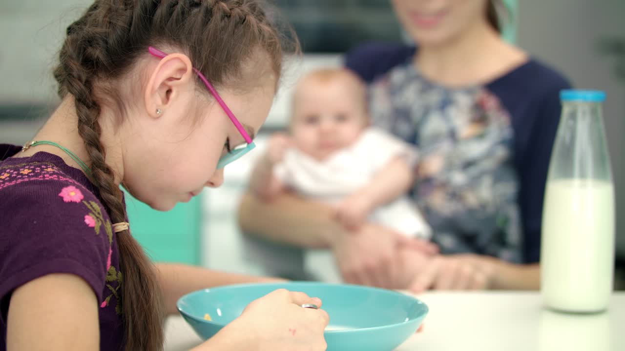 Una bambina fa colazione con la madre e il bambino. La bambina pranza in cucina.