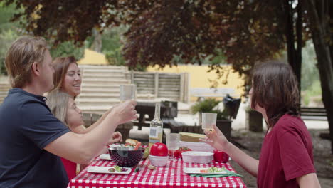 Happy-Caucasian-family-clinking-glasses-during-a-picnic-in-the-forest