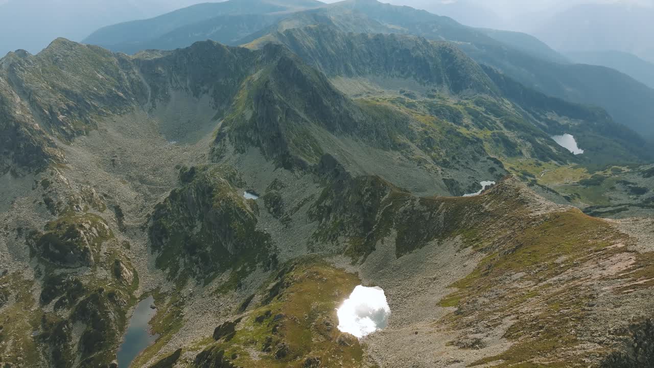Multiple glacial lakes spread across tall mountain ranges, surrounded by vibrant green pastures, top aerial view