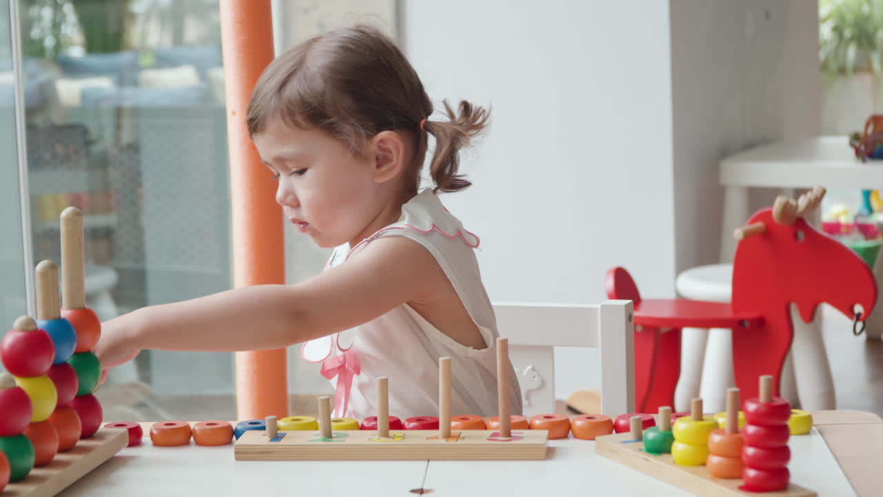 niña jugando con el recuento de anillos apilando juguetes en el interior sentada junto a la mesa - cámara lenta