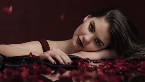 retrato hermosa mujer caucásica jugando con pétalos de rosa cayendo sensual mujer soñando con fantasía íntima romance indulgente deseo en fondo rojo concepto del día de san valentín