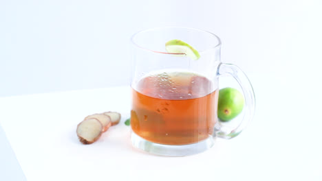 té de limón en una taza de vidrio transparente con hojas de menta de limón enteras y en rodajas en un plano lateral giratorio de fondo blanco