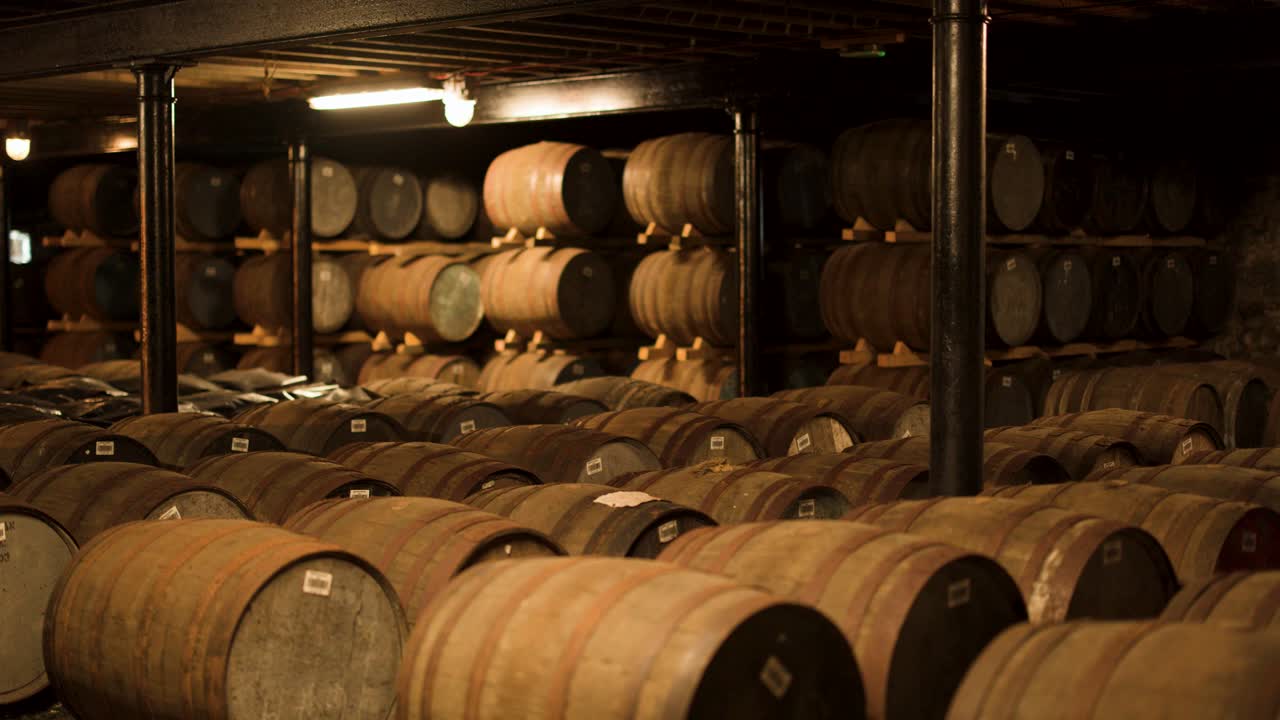 Wooden whisky barrels aging in a dim, rustic stone warehouse with a slow camera pan