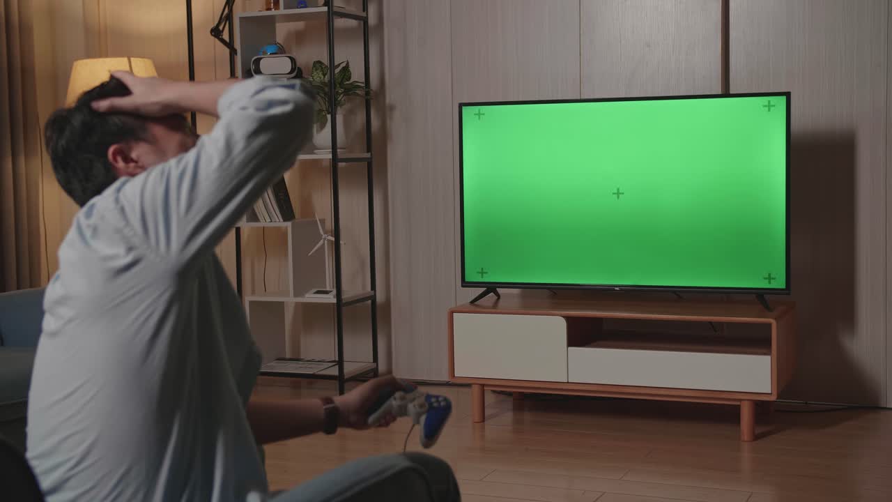 Gamer maschio deluso per aver perso una partita, che gioca a un videogioco con una TV a schermo verde a casa.