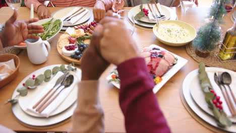 happy diverse senior friends holding hands to say grace at christmas dining table, slow motion