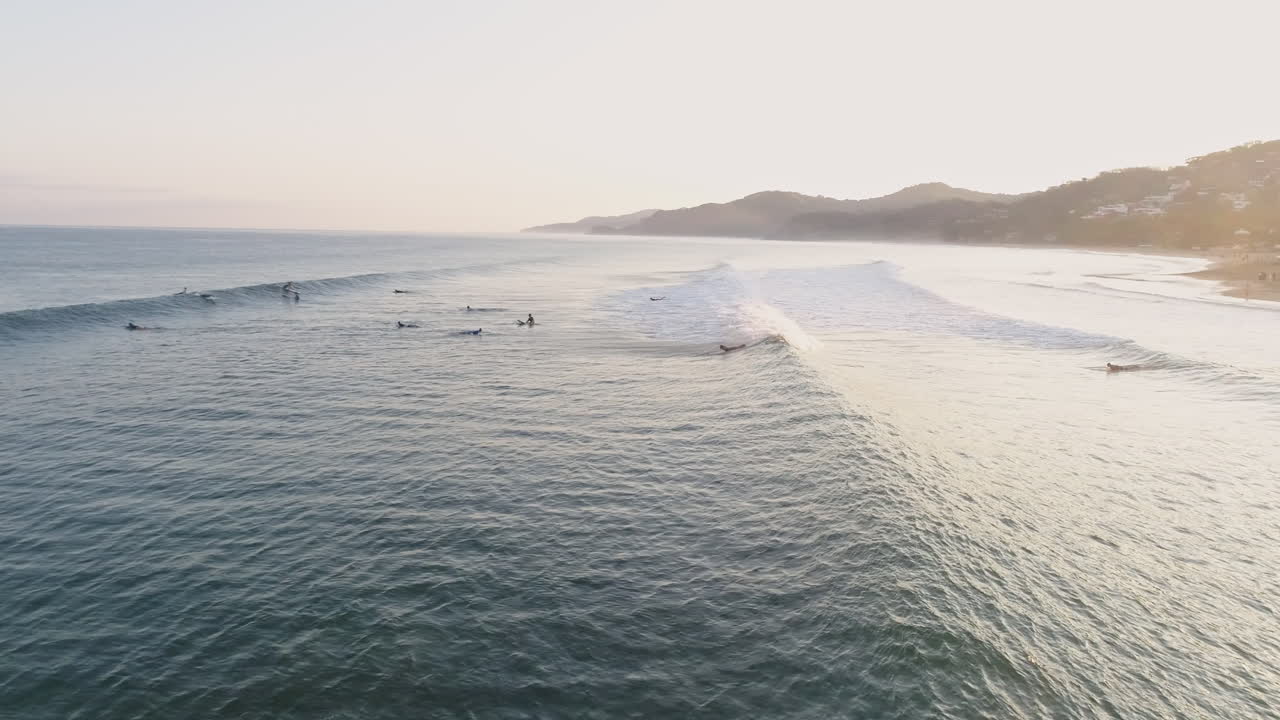 Aerial as surfers paddle out during beautiful sunrise tropical coast, 4K