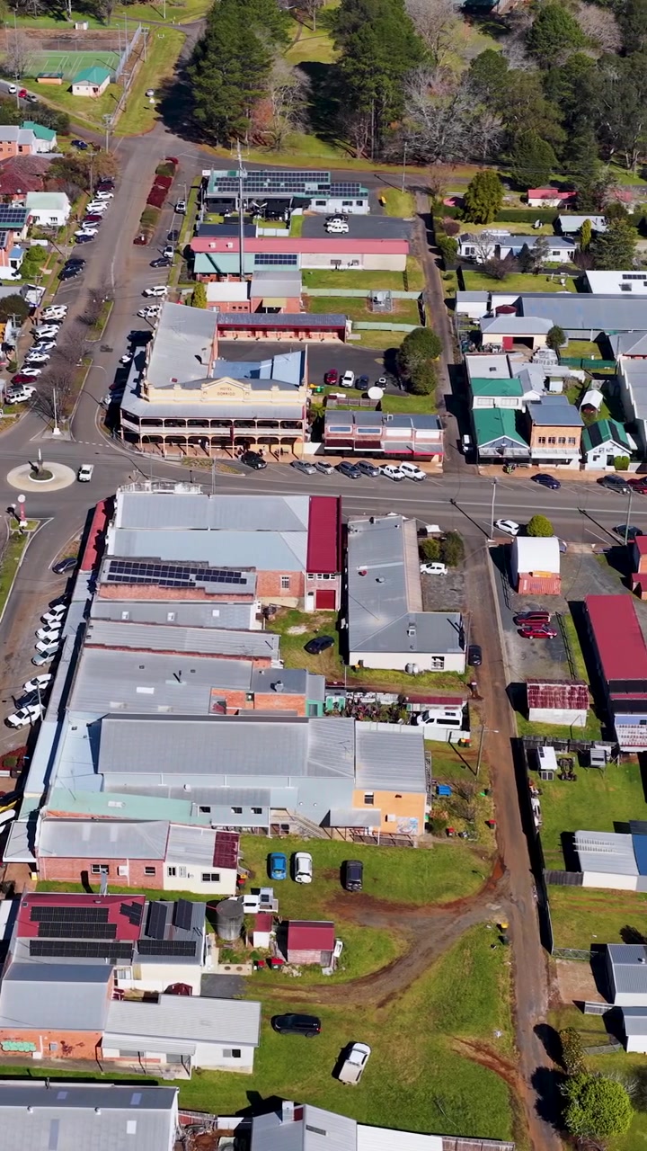 Drone stiger op over Dorrigo by og afslører gader, butikker, huse og landskab i dagslys.