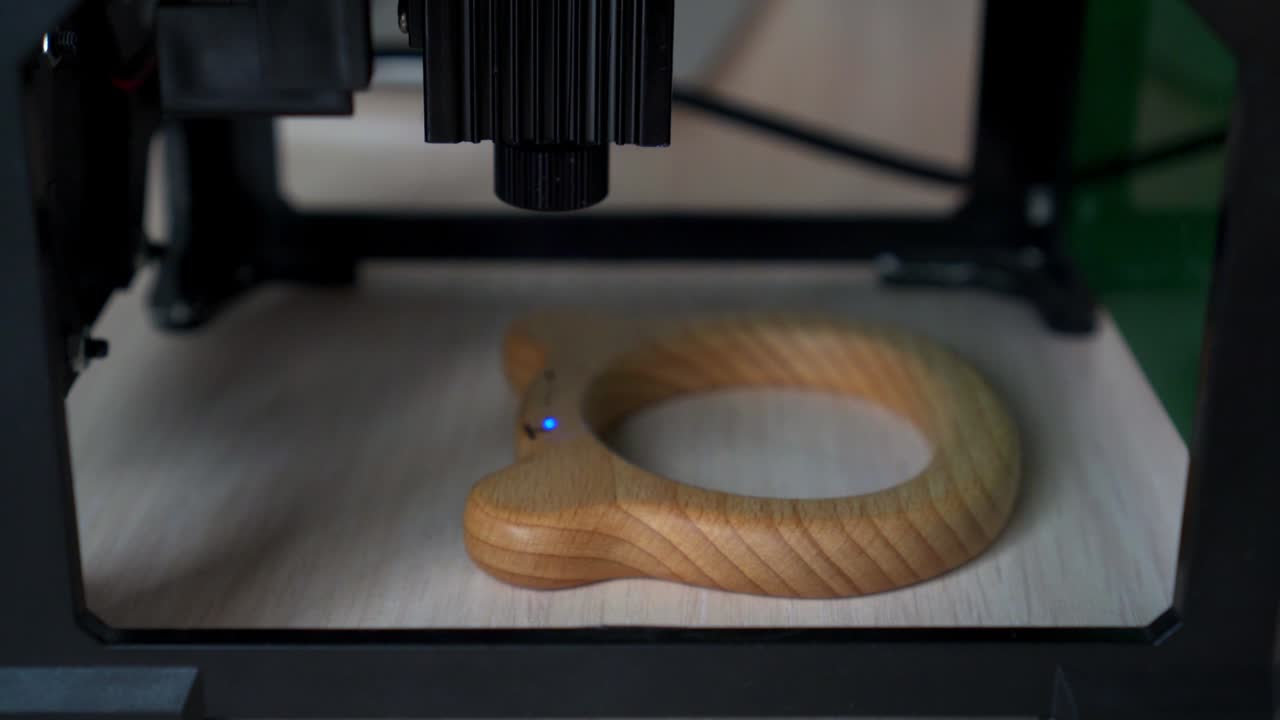 Desktop laser wood burning machine uses a blue laser beam to inscribe name on surface of childrens wooden toy. Home production of teethers and rattles for babies