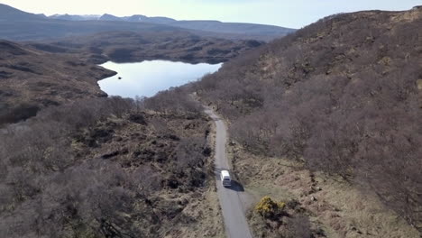 aerial footage of a vintage vw campervan driving down a country road on a sunny day in assynt, scottish highlands, scotland