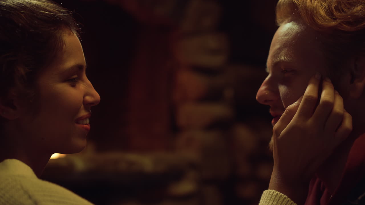 여자친구 남자친구가 벽난로 옆에서 얼굴을 만집니다. 사랑스러운 커플은 저녁에 바람을 피운다.