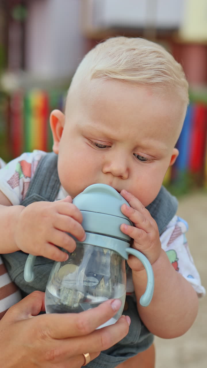 Un bambino di 10 mesi beve acqua da una tazza con cannuccia. Il bambino beve acqua.