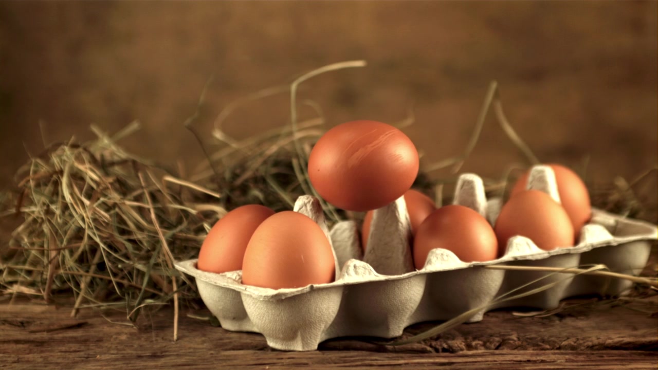 Kartong med ferske brune egg plassert på et rustikt trebord med høy