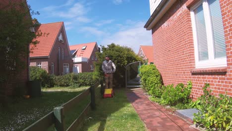 Young-man-cutting-the-grass-with-the-lawn-mower-in-front-of-the-house-and-talking-to-his-neighbours