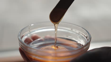 honey flowing in slow motion from a wooden stick into a glass bowl