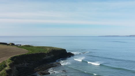 Circular-aerial-footage-of-a-beautiful-part-of-Ireland-with-cliffs,-agricultural-field,-sandy-beach,-green-grass