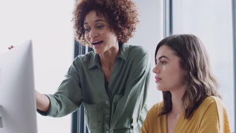 Two-female-creatives-discussing-a-project,-looking-at-a-computer-screen-in-an-office,-close-up