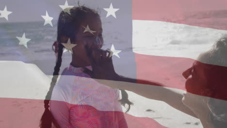 animation of flag of united states of america over biracial mother with daughter on beach