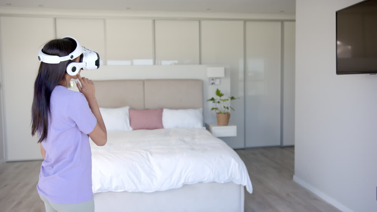 Using VR headset, woman exploring virtual reality in modern bedroom, copy space