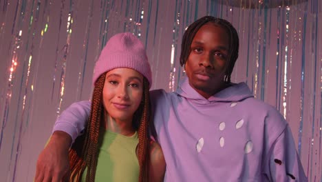 Studio-Portrait-Shot-Of-Young-Gen-Z-Couple-Standing-In-Front-Of-Tinsel-Curtain-Against-Pink-Background