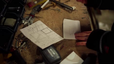 man draws on piece of paper in the wood workshop table