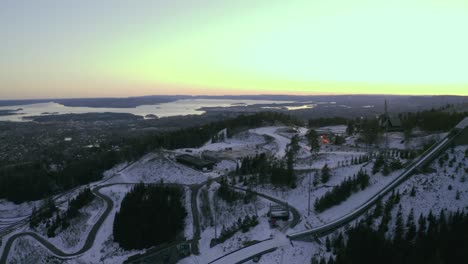 Ciudad-De-Oslo-Con-Salto-De-Esquí-Holmenkollbakken,-Parque-De-Invierno-Parque-De-Invierno-Tryvann-Drone-Envuelto-Alrededor-Del-Salto-De-Esquí-Al-Atardecer-Holmenkollen