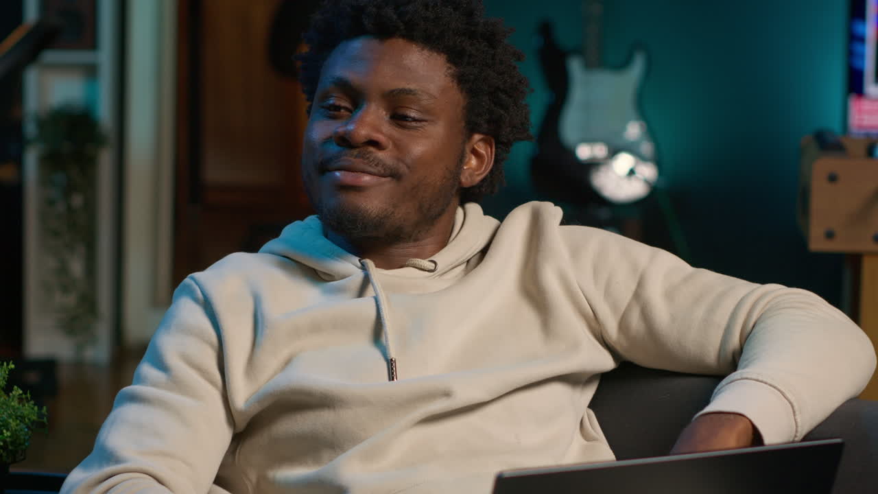 Black man does his research by reading articles and taking notes at home, collecting information for a new project. Freelancer multitasking and studying files with data driven papers. Camera A.