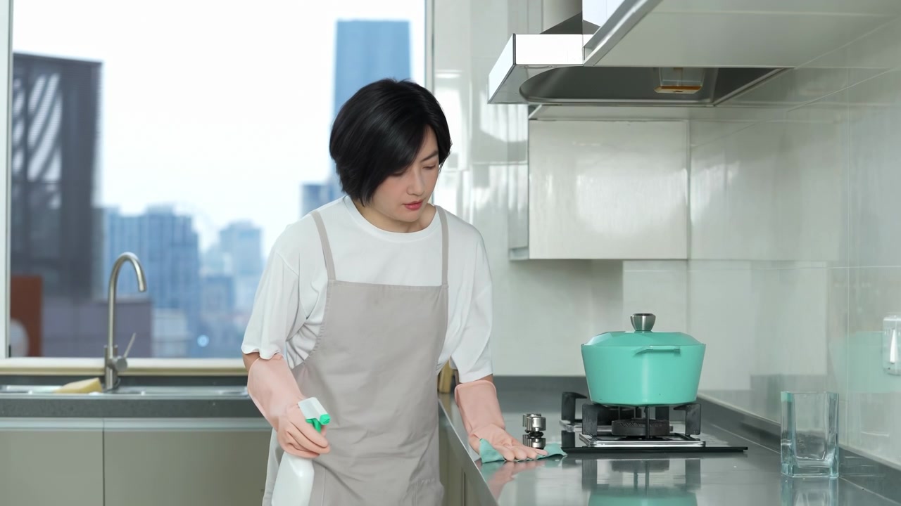Người nội trợ tập trung đeo găng tay cao su bảo hộ đang lau dọn tủ bếp, bàn bếp bằng giẻ để loại bỏ bụi bẩn, vi khuẩn hoặc mầm bệnh, sử dụng bình xịt và miếng bọt biển tẩy rửa; người phụ nữ đang làm việc nhà tại nhà.