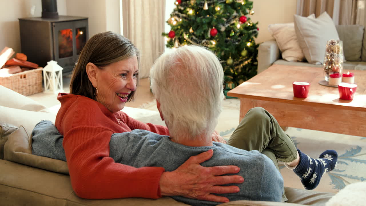 Senior couple laughing together at home near Christmas tree, feeling joyful