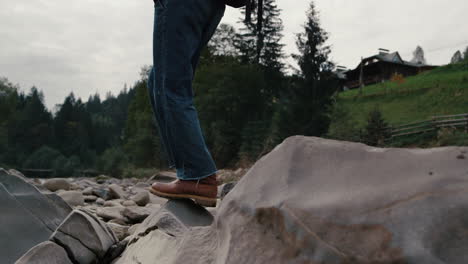 man in boots hiking on rocks at river. male hiker walking in summer mountains