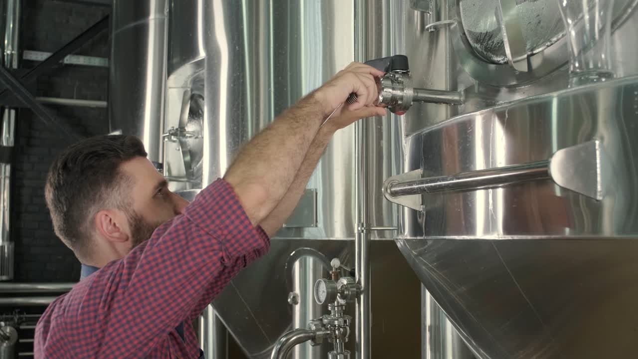 un joven cervecero con un delantal de cuero supervisa el proceso de fermentación de la cerveza en una fábrica de cerveza moderna
