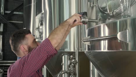 young male brewer wearing a leather apron supervise the process of beer fermentation at a modern brewery factory