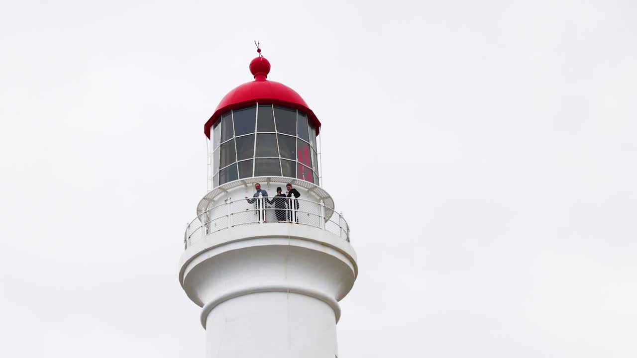 A lighthouse with a red top stands against a cloudy sky, captured from various angles, highlighting its architectural details